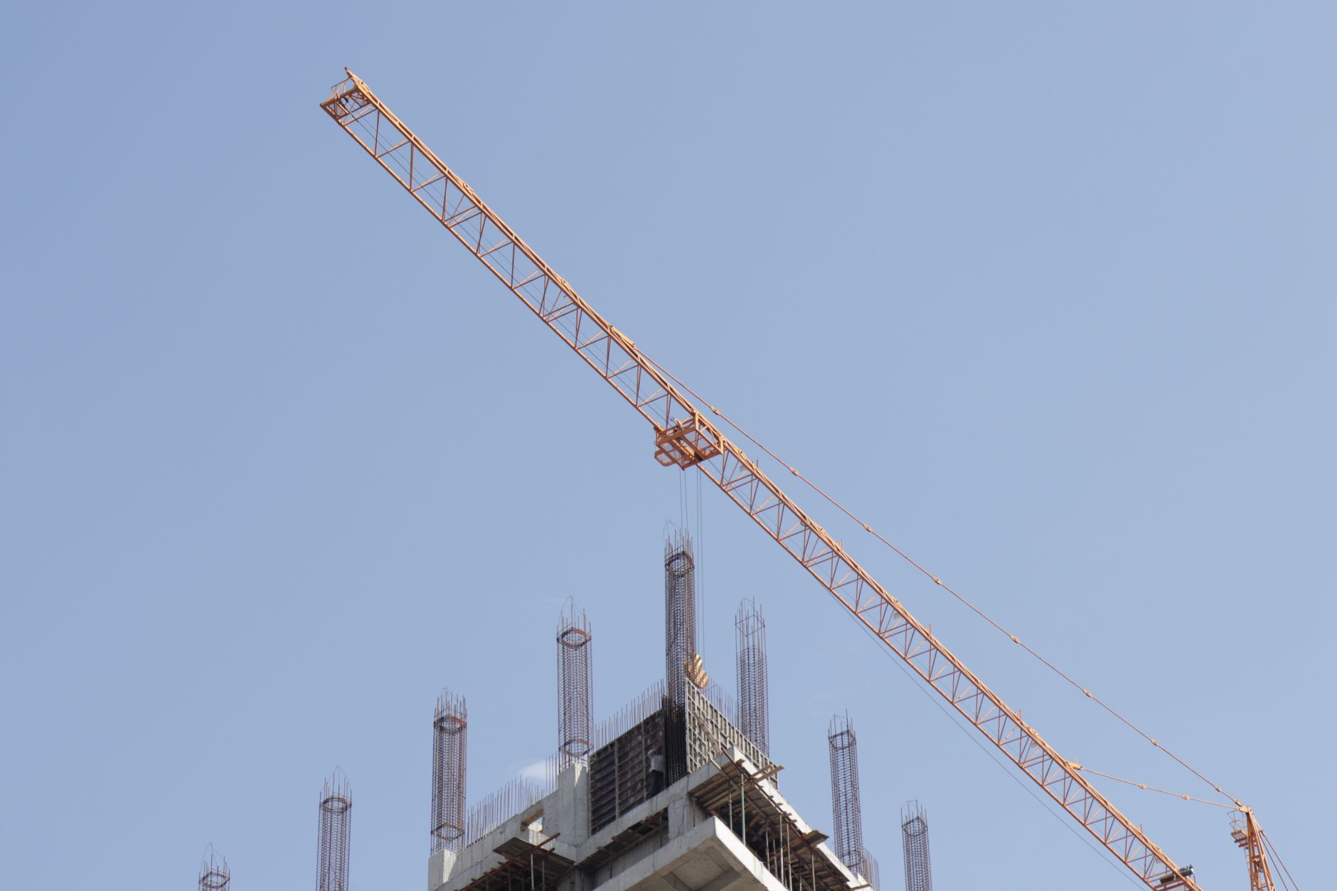 青空の下、高層建築の工事現場で稼働するタワークレーン
