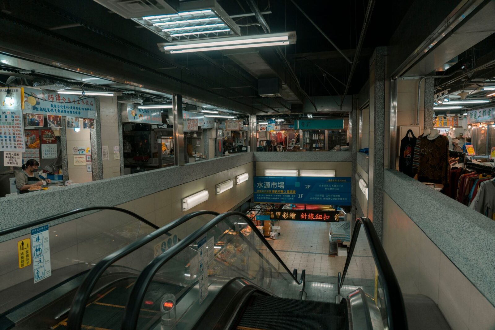 Interior view of a modern shopping mall with escalators and retail shops.